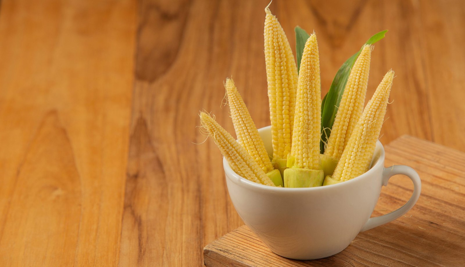 baby corn is placed in a glass on a wooden floor.