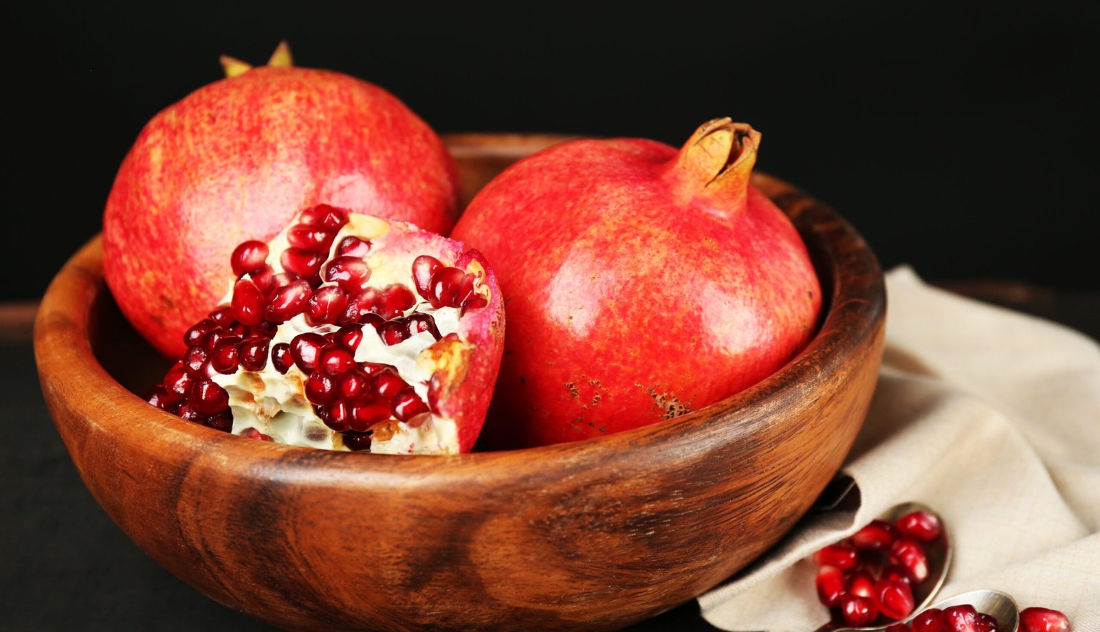 Juicy ripe pomegranates on wooden table, on dark background